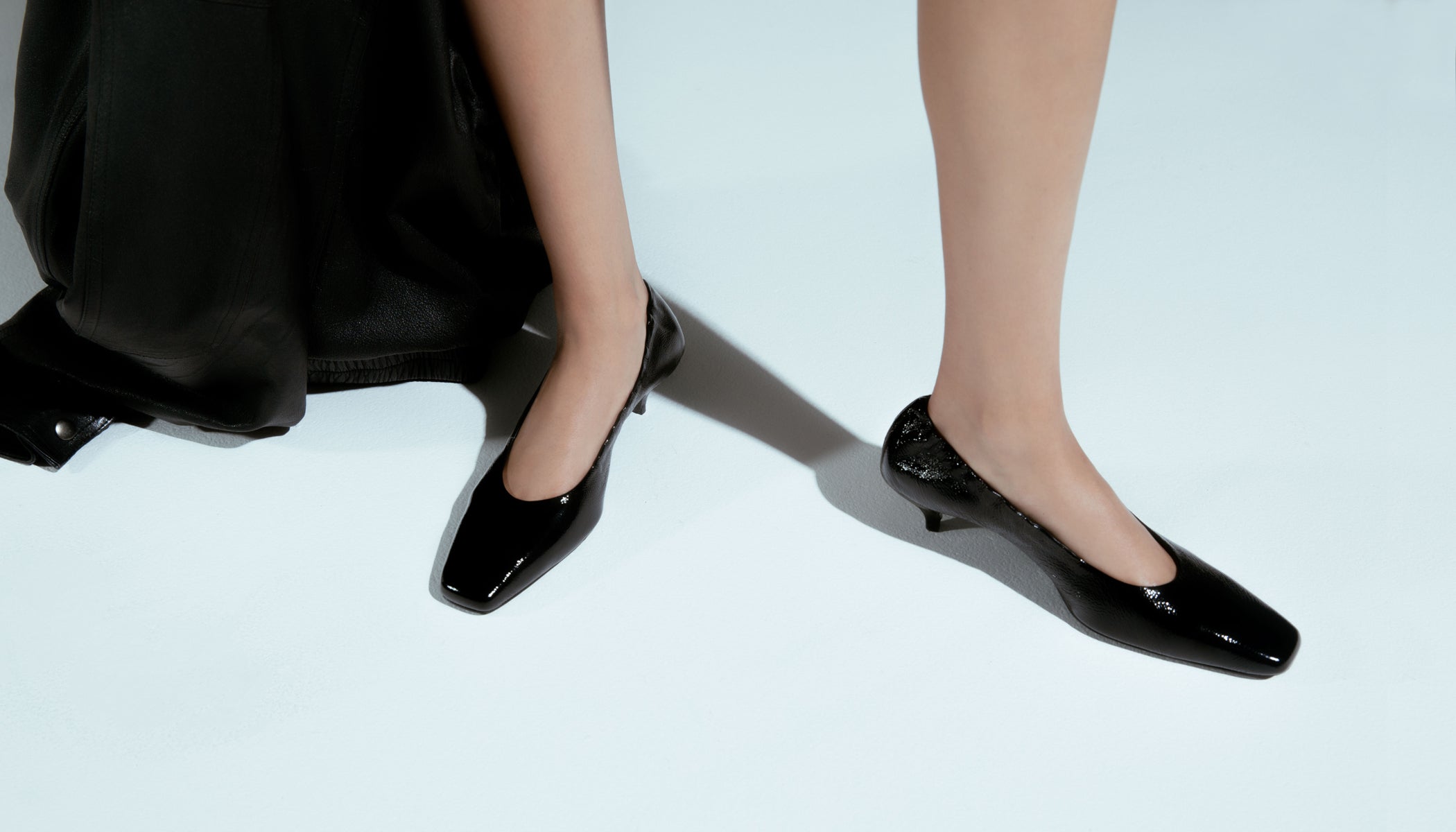 Black patent leather shoes worn by a person on a light background