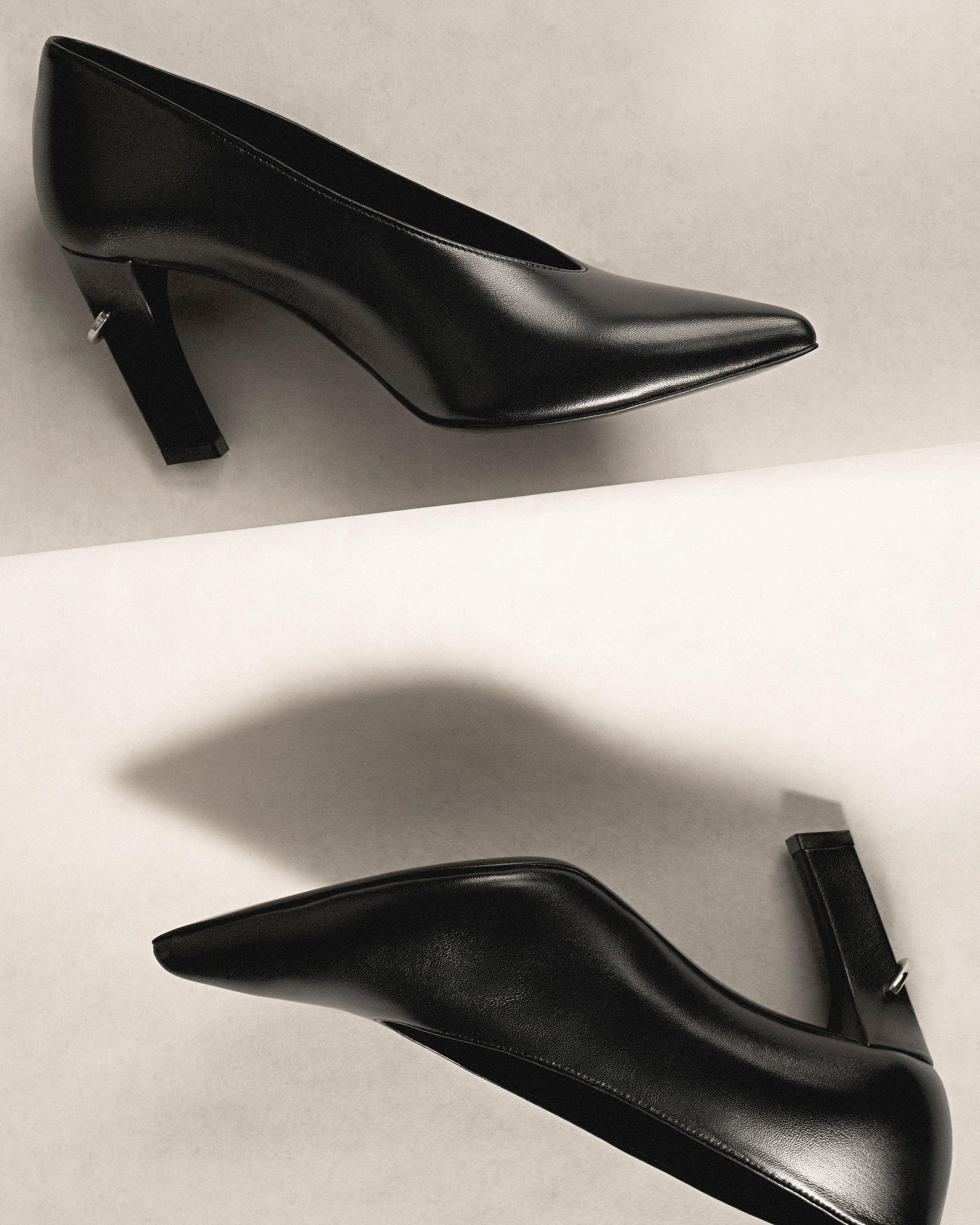 Pair of black high-heeled shoes with piercing details on a light gray background