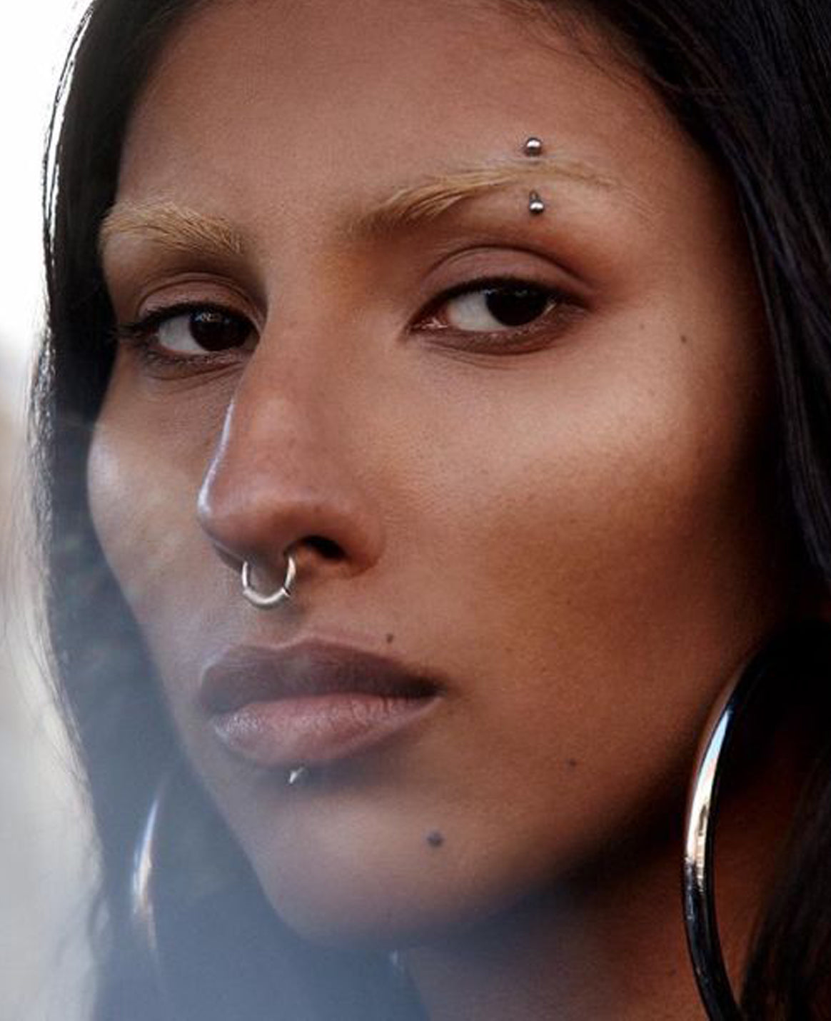 Close-up of a person with multiple piercings on their face and ears.