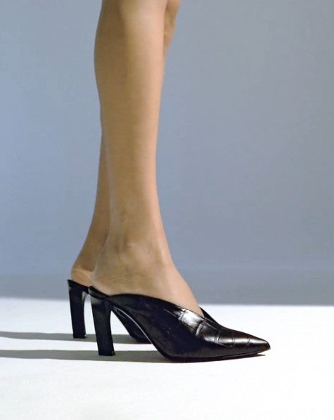 Black mules with crocodile effect wearing by model making two steps